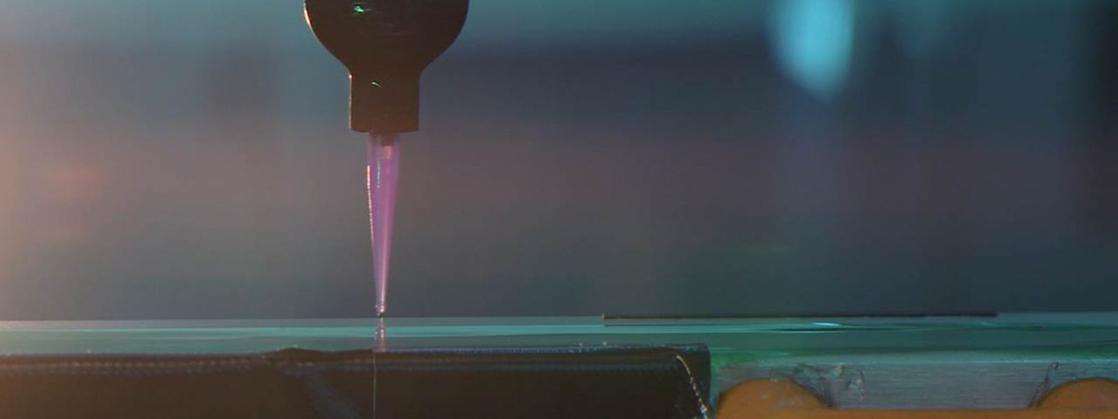 Seitliche Ansicht einer Dosierdüse beim Auftrag von silikonbasiertem Optical-Bonding-Material auf eine Displaykomponente